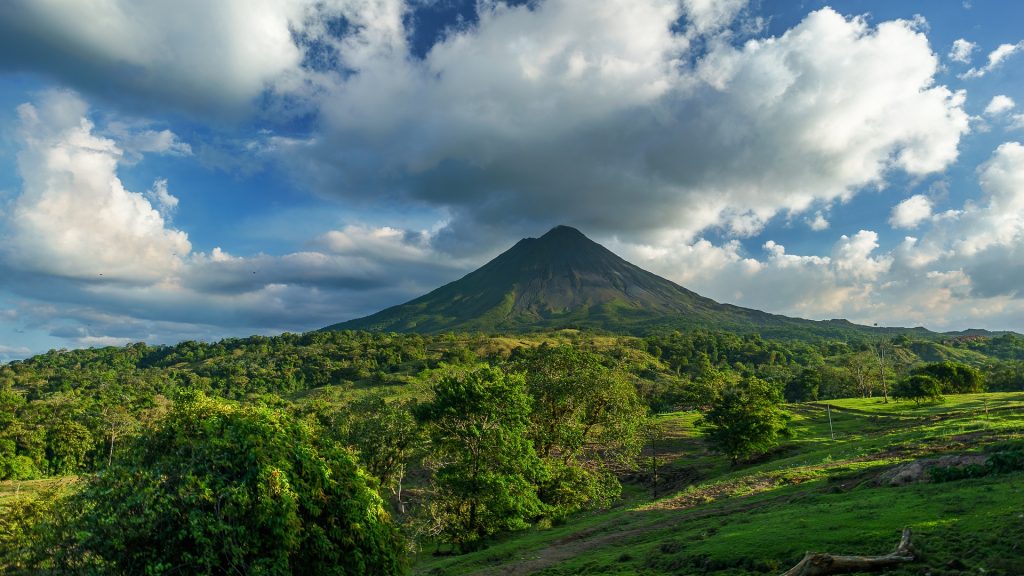 a vulcano in costa rica with green grass and mountains in the background