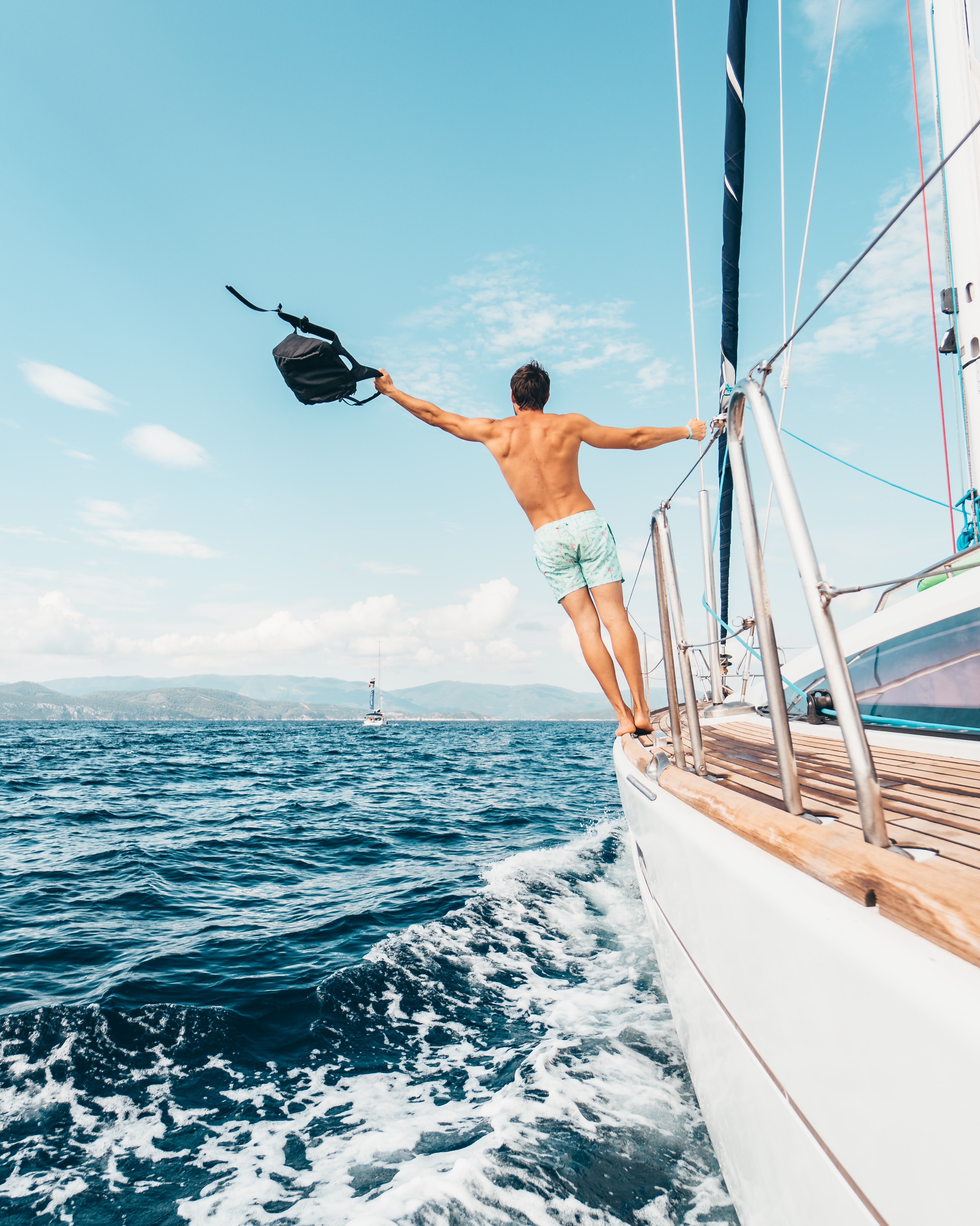 The top sailing spots this summer with a man on a sailing boat swinging a black bag